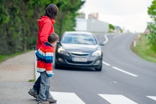 photo of a mother and a son crossing the street in a crosswalk with an approaching car 